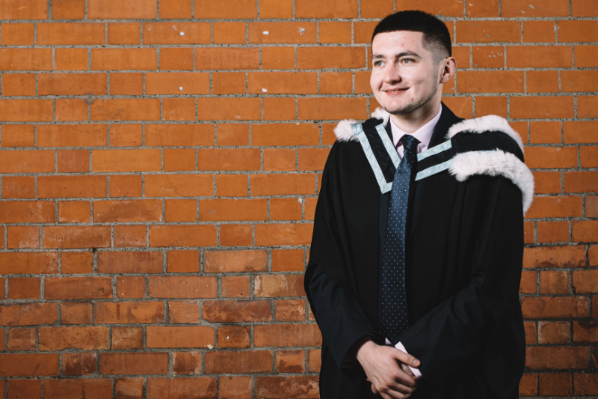 male student standing with graduation gown on