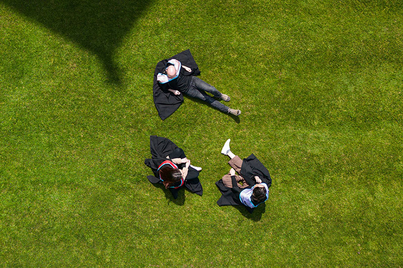 Three students in Graduation gowns in the quad