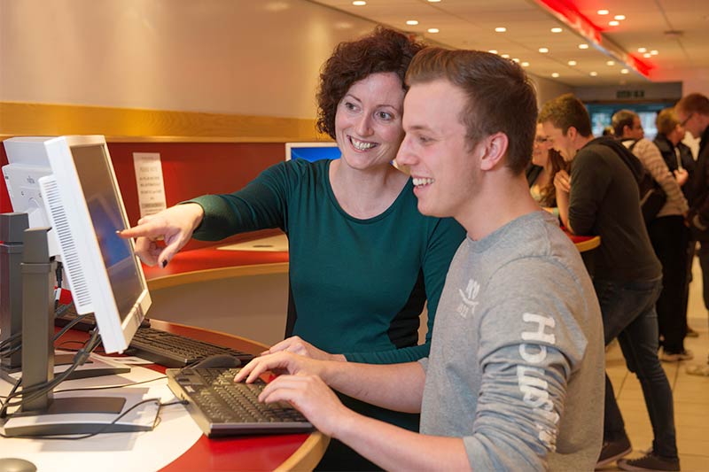 member of staff assisting student on a computer