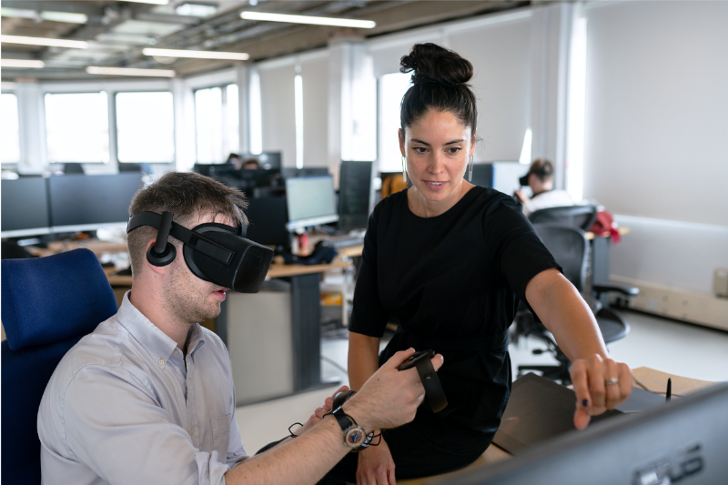 A man uses a VR headset and his colleague supervises