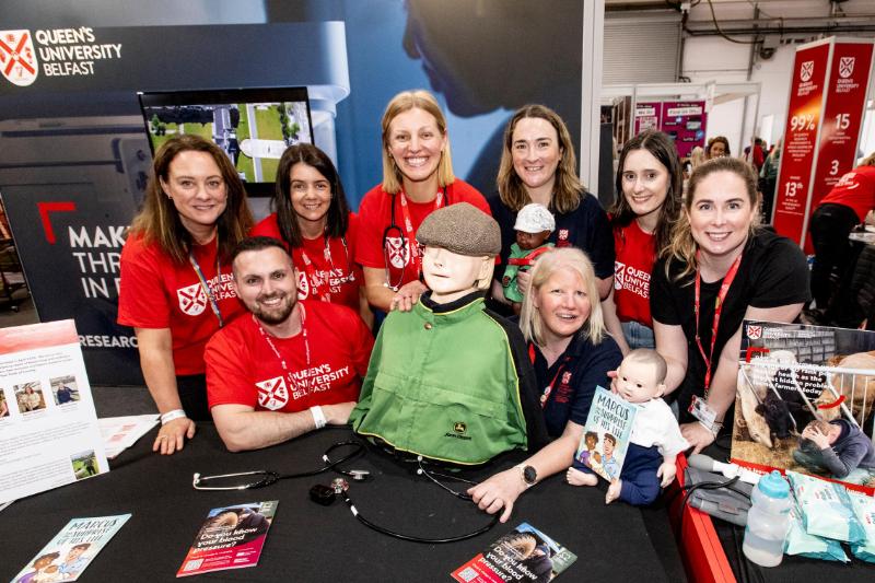 Queen's University Belfast staff in red Queen's-branded t-shirts posing with a mannequin at an exhibition stand at the 2024 Balmoral Show