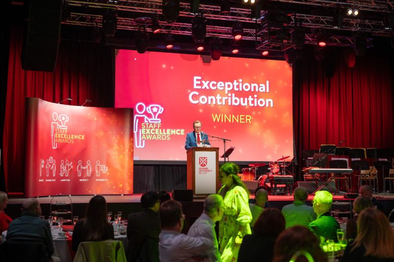 Image shows Professor Ian Greer on the stage at the 2022-23 Staff Excellence Awards. Behind him the screen reads: Exceptional Contribution WINNER