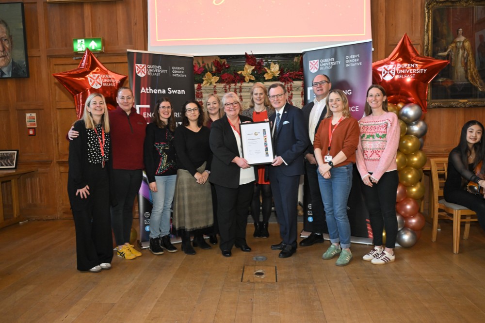 group of people collecting an award in an old wood-paneled event hall with pop-up stands, balloon pillars and presentation screen in the background