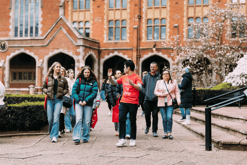 group of people following a tour guide outdoors, with flower blossoms and old redbrick building pictured in the background