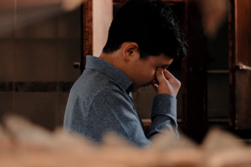profile of stressed- or upset- or tired-looking young male with his head down and hand up to his face