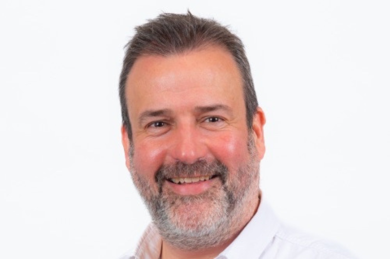 Headshot of a smiling man with short dark hair and a beard against a plain light background
