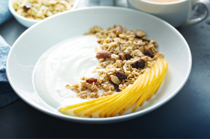 yogurt, granola and sliced apple or pear in a bowl on a table