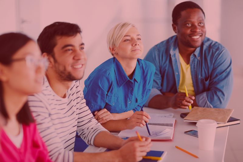 small group of smiling people with notebooks and pens sitting in a training or information session