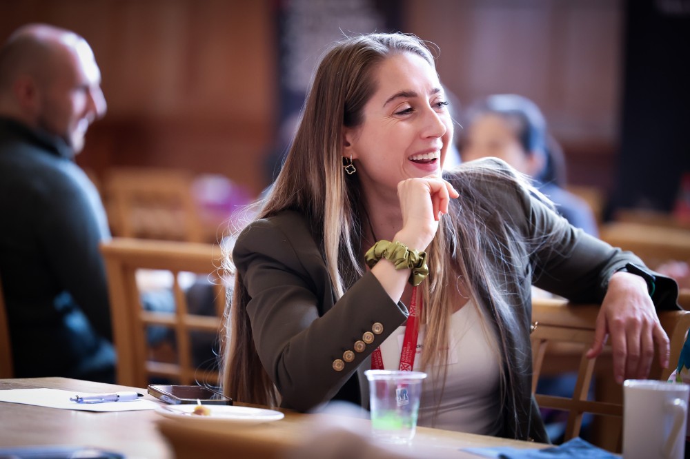 professional-looking woman wearing red lanyard smiling and seated at an event table