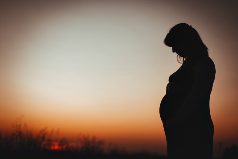 pregnant woman silhouetted against a dusky, late evening sky