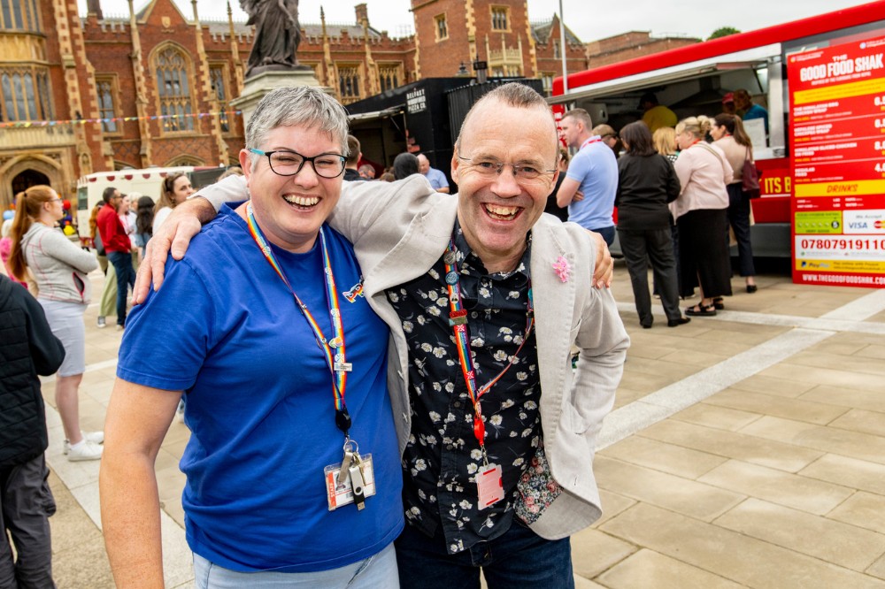 two staff members smiling to camera beside the food trucks outside Queen's Lanyon Building at the Pride Picnic 2024