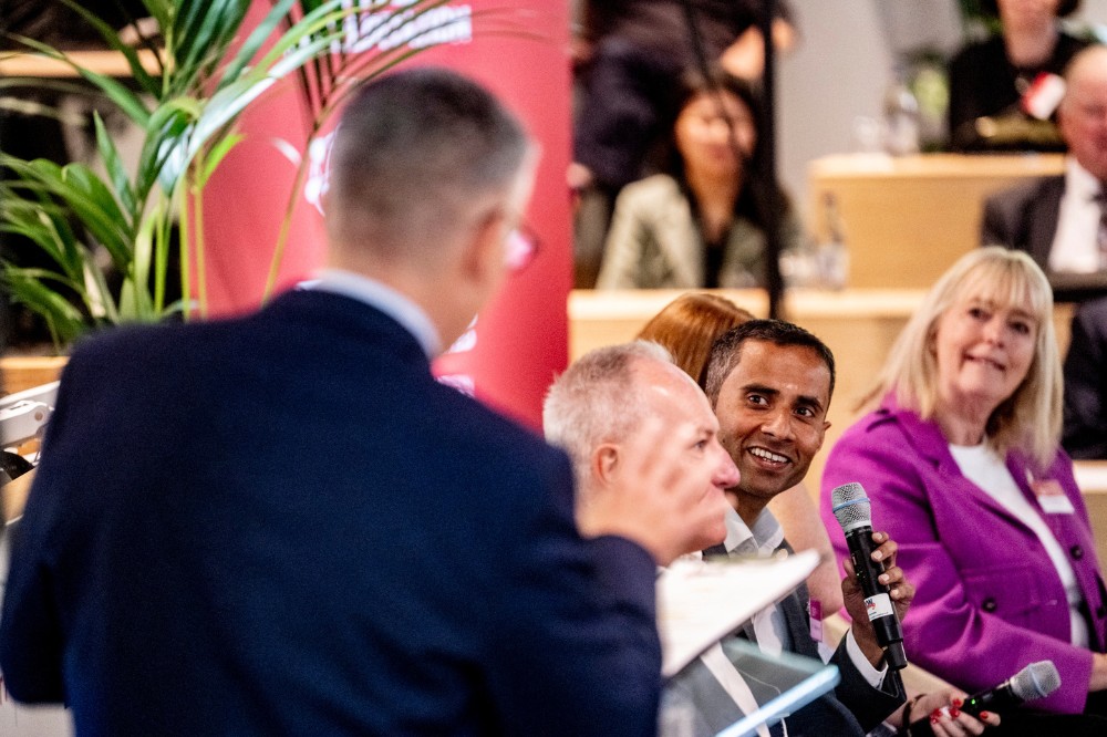 a seated group of event panelists smiling at the event emcee whose back is turned to the camera
