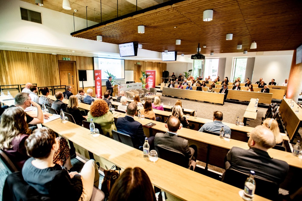 bright, modern lecture hall viewed from the back with seated guests shown listening to a presentation or panel interview