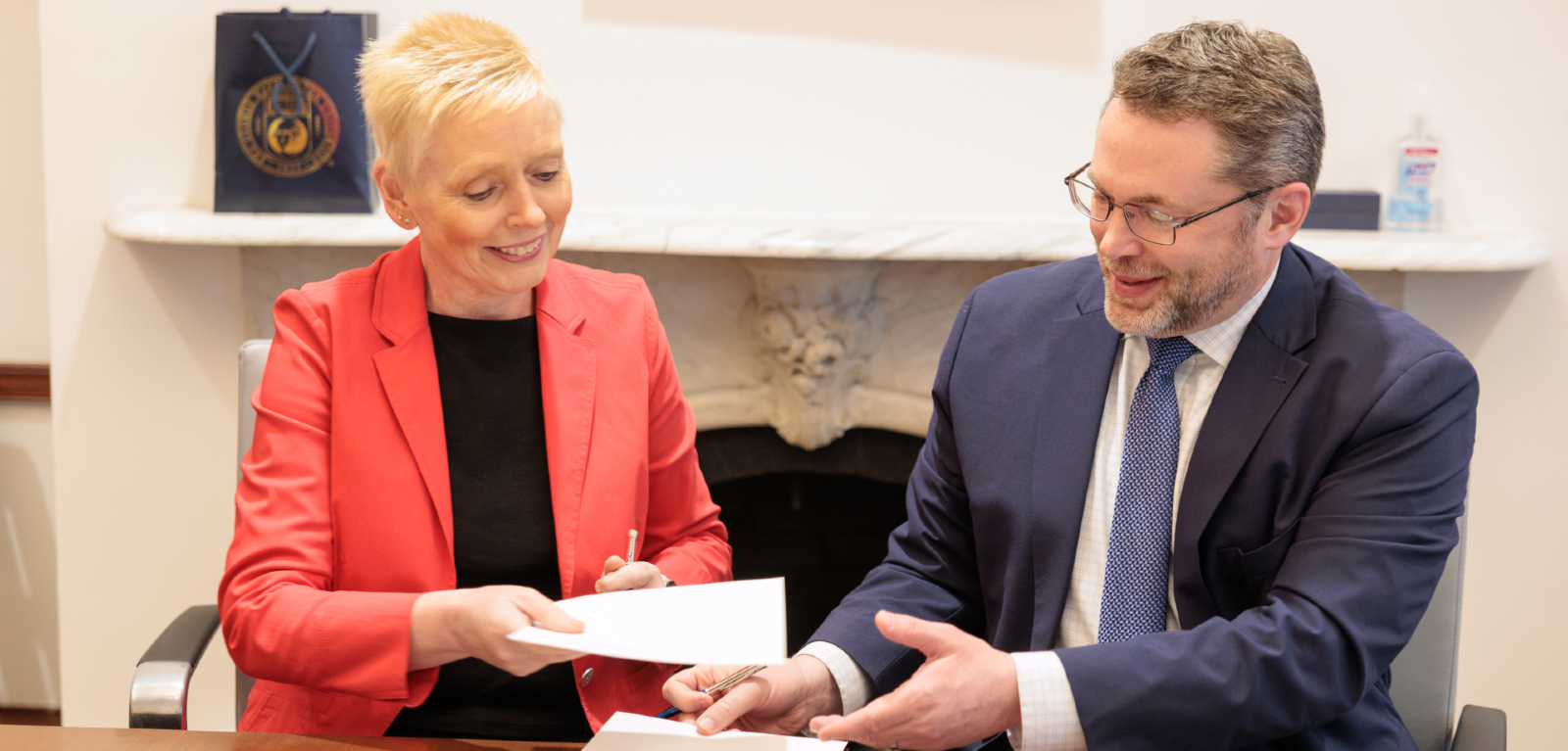 A woman and man sign documents at a college campus