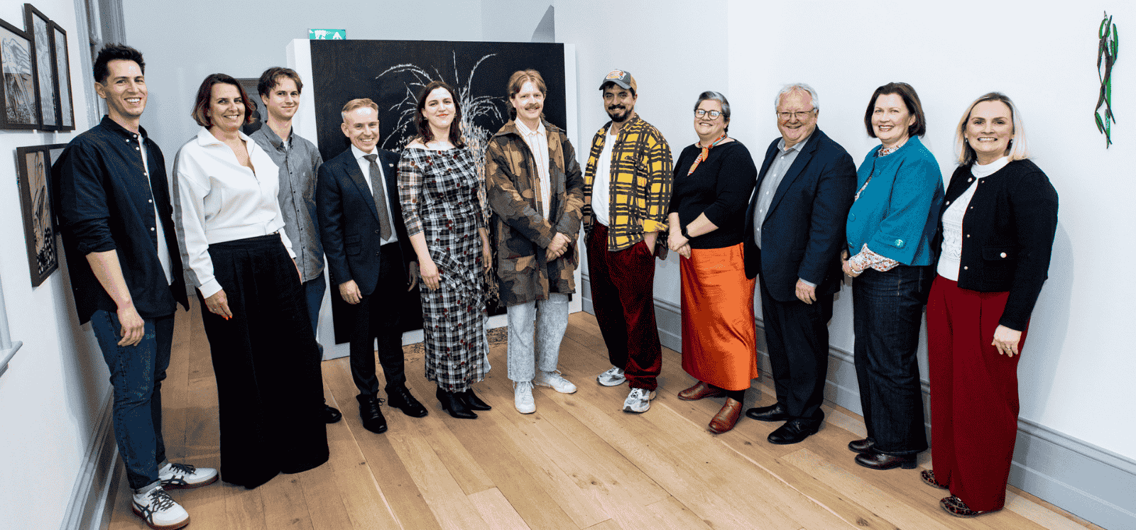group of smiling people standing side by side posing for the camera in an art gallery