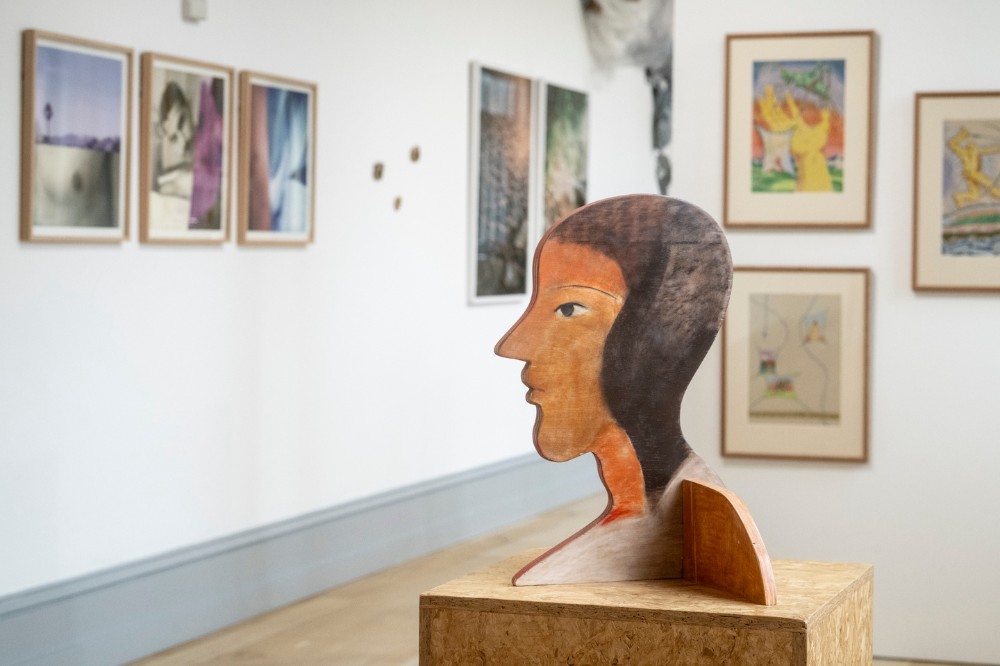 sculpture of a woman's head pictured in the middle of an art gallery with various other artworks displayed in the background