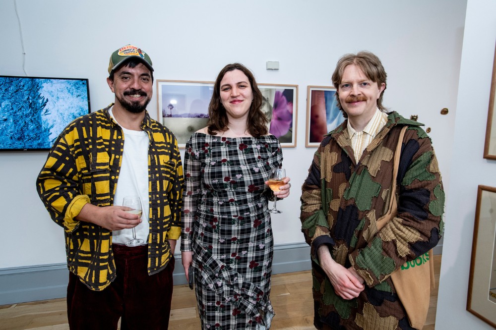 woman and two men smiling for the camera in an an art gallery