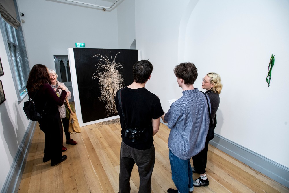 art gallery visitors looking away from the camera chatting about an artwork in the background
