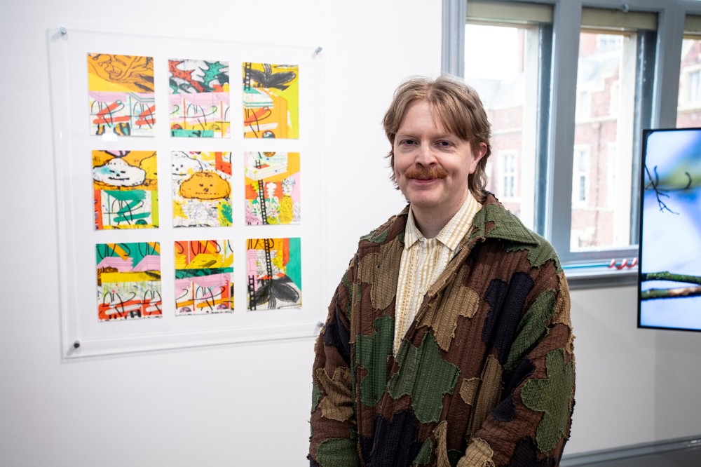 smiling man posing beside an artwork hung on an art gallery wall