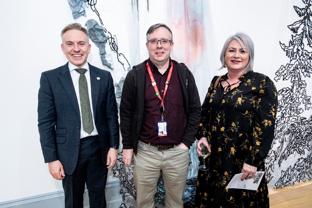 woman and two men smiling for the camera in an an art gallery