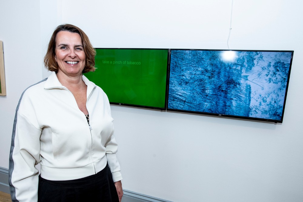 smiling woman pictured beside an artwork displayed on a gallery wall