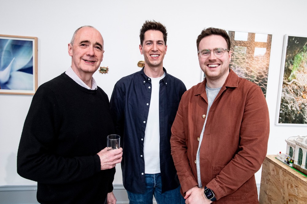 three men smiling for the camera in an art gallery