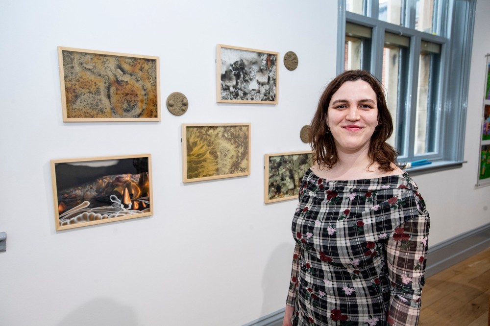 smiling young woman posing beside various small artworks pinned to a wall