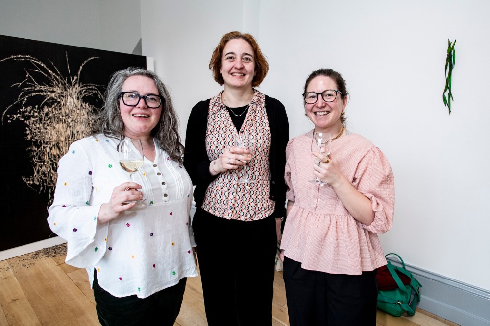 three women smiling for the camera in an art gallery