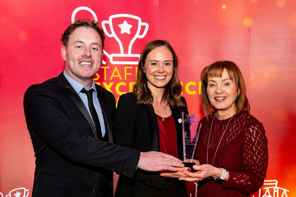smiling woman being presented with a crystal trophy by a man and woman at an indoor event