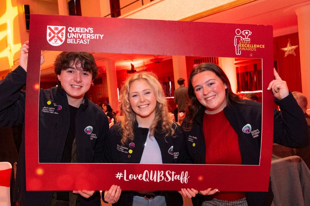 one young man and two young women wearing nearly-matching branded zip-up tops posing with an Instagram photo frame cutout