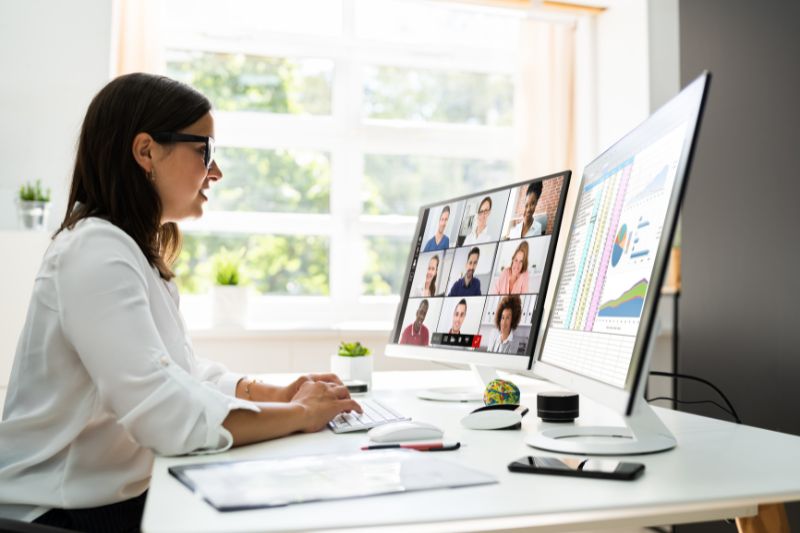 woman seated at desk in bright office space joining a webinar on two computer screens