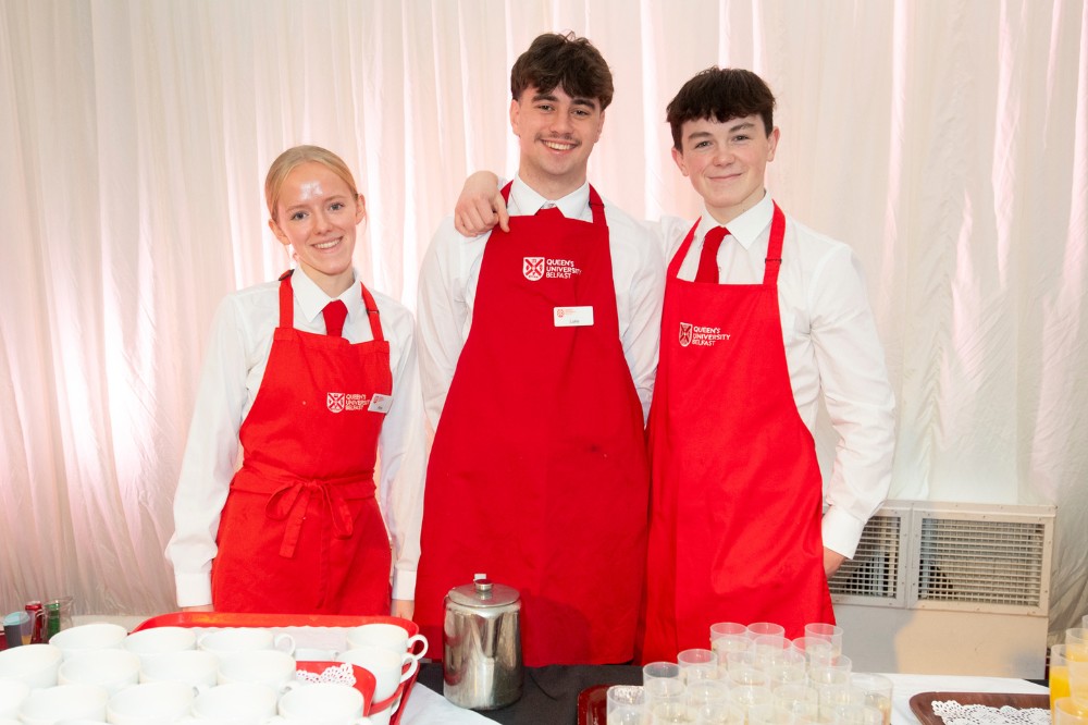 two young men and a young woman - catering staff - in white shirts and red aprons posing for the camera in an event marquee