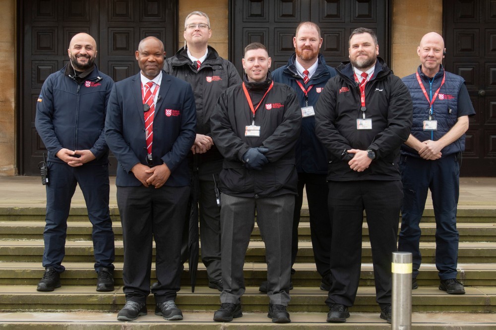 group of smiling security personnel standing at the steps of a large hall in the background